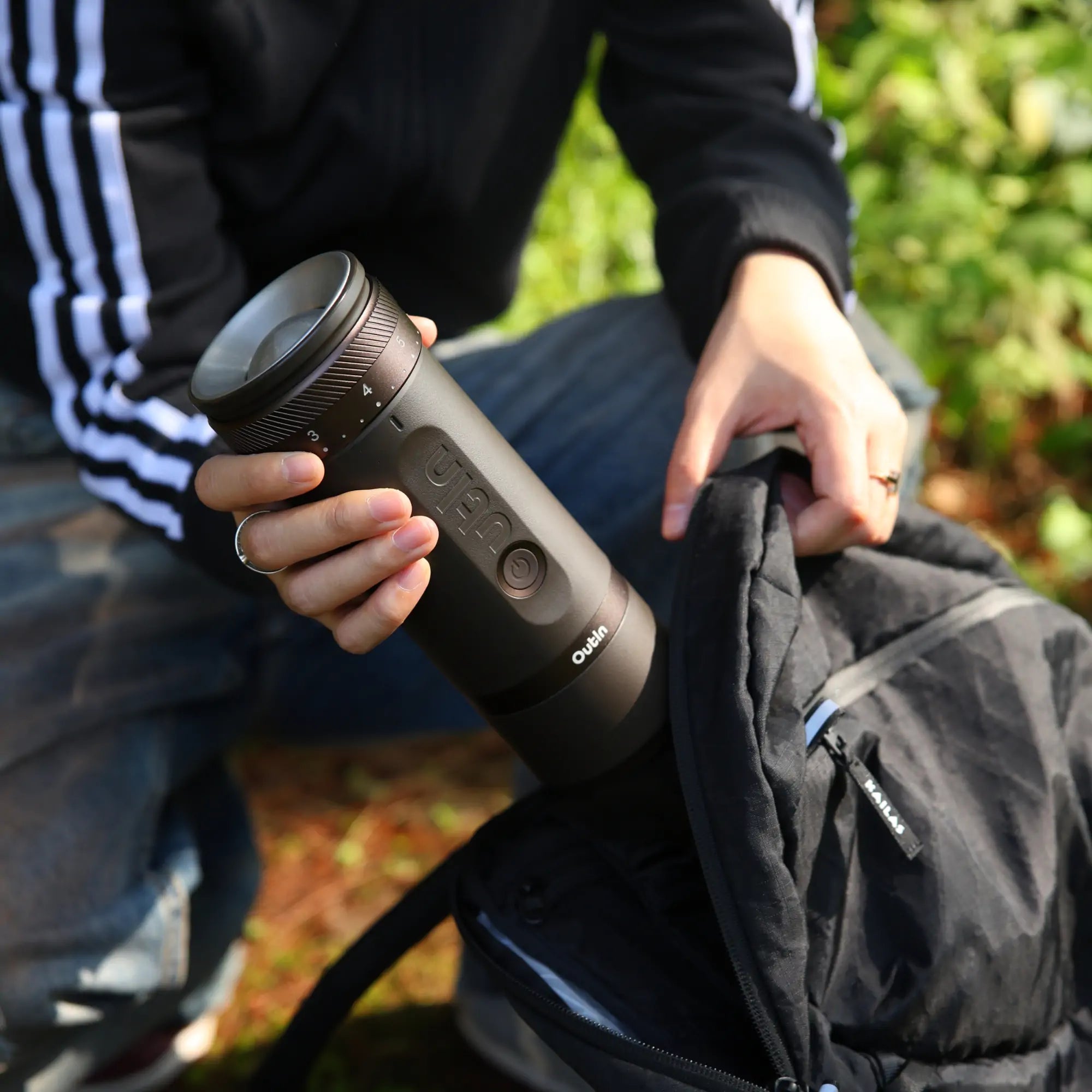 Outin Fino portable electric coffee grinder being placed in backpack for outdoor use