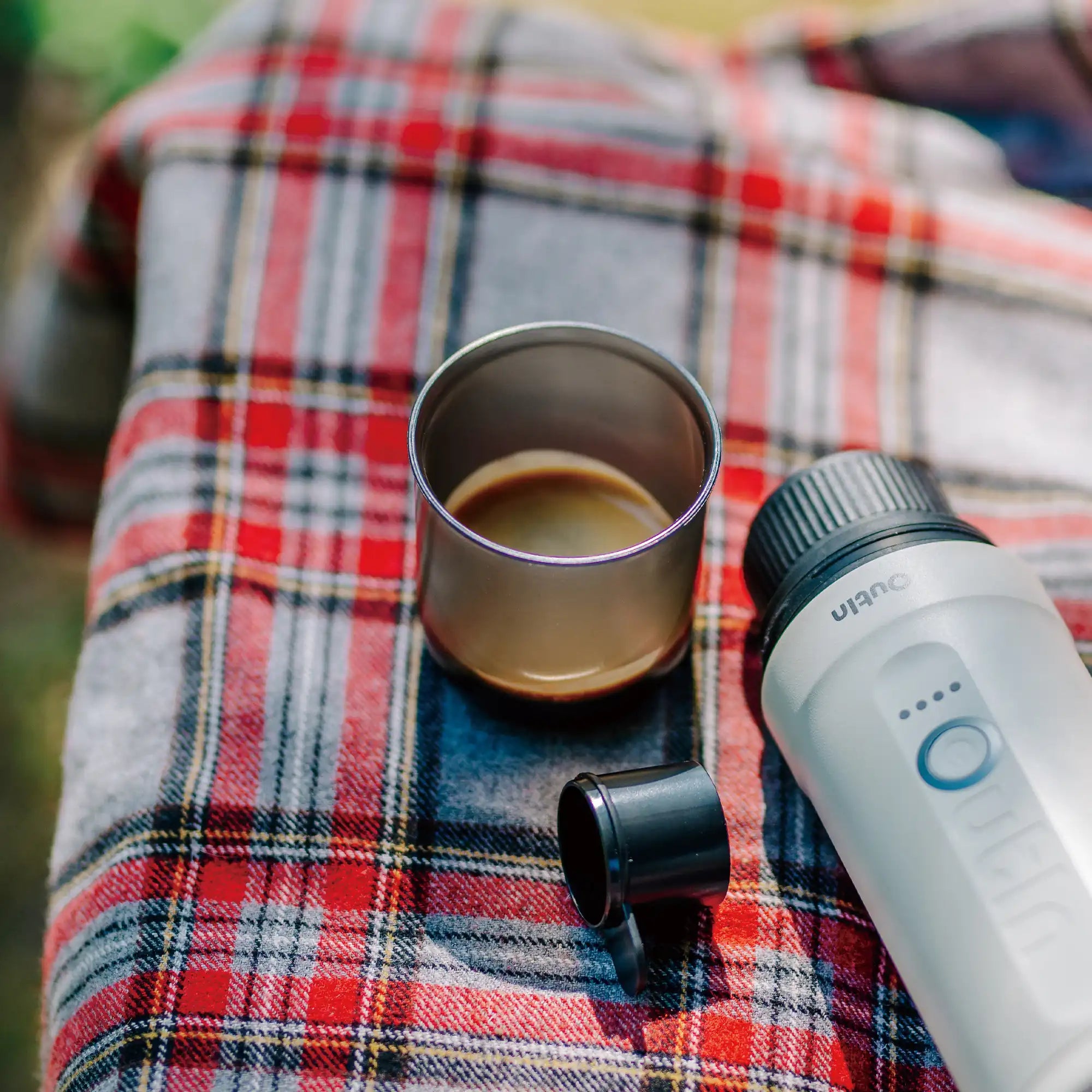 Dark espresso cup beside Nano Portable Espresso Machine outdoors.